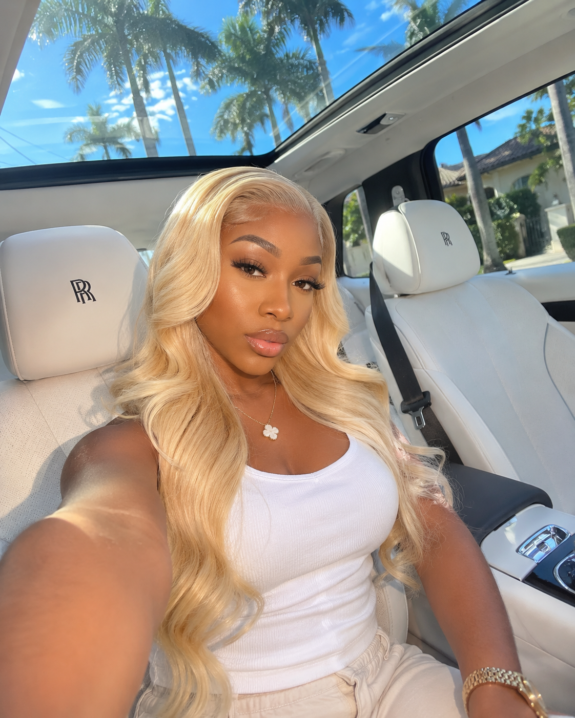 Woman with long blonde hair sitting inside a luxury car with palm trees in the background